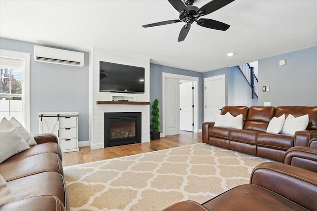 living area with wood finished floors, baseboards, a wall unit AC, a large fireplace, and a ceiling fan