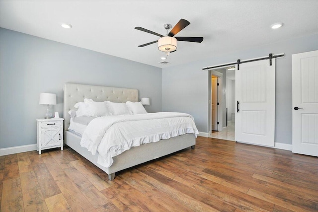 bedroom with recessed lighting, baseboards, a barn door, and hardwood / wood-style floors