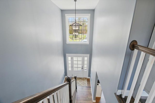 stairway with baseboards, wood finished floors, and a notable chandelier