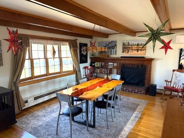 dining space with a brick fireplace, beamed ceiling, a baseboard heating unit, and wood finished floors