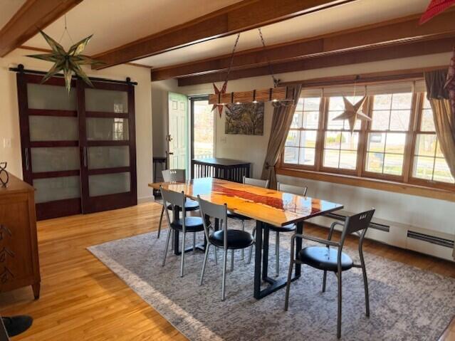 dining space with a barn door, wood finished floors, and beamed ceiling