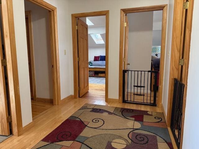 corridor with baseboards, wood finished floors, and a skylight