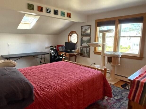 bedroom featuring a baseboard heating unit, lofted ceiling with skylight, and wood finished floors