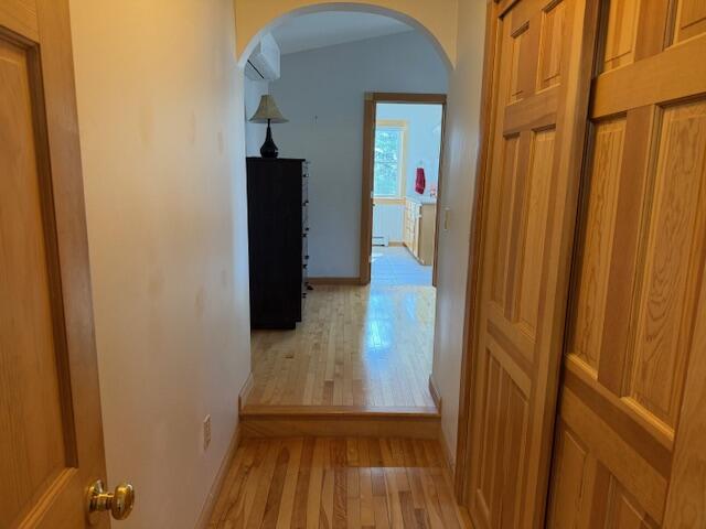 hallway featuring arched walkways, baseboards, and light wood-style flooring