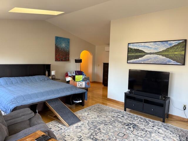 bedroom featuring arched walkways, baseboards, wood finished floors, and lofted ceiling