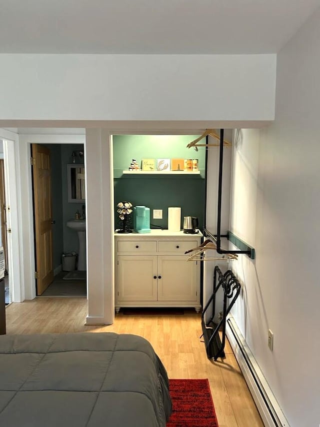 bedroom featuring light wood-style floors, a baseboard radiator, and connected bathroom