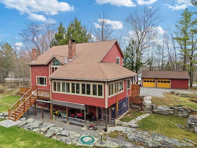 rear view of house with stairs, a garage, a sunroom, an outbuilding, and a chimney