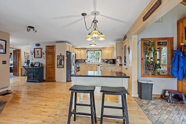 kitchen with decorative light fixtures, appliances with stainless steel finishes, tasteful backsplash, light wood finished floors, and cream cabinetry