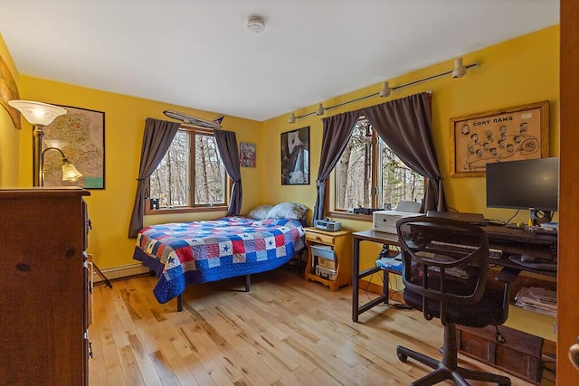 bedroom with baseboard heating, multiple windows, and wood finished floors