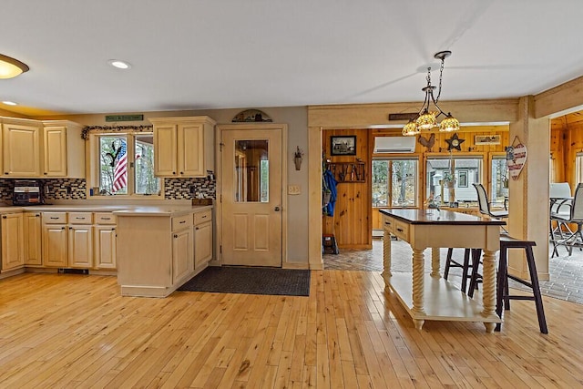 kitchen with light brown cabinetry, light wood-style floors, a wall mounted air conditioner, decorative light fixtures, and backsplash