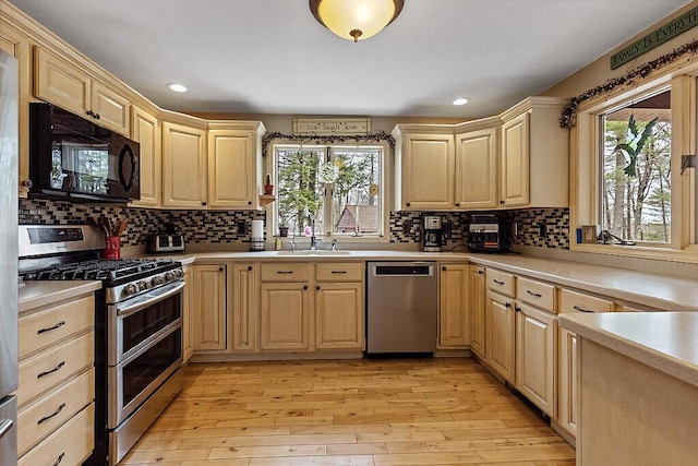 kitchen featuring light brown cabinetry, a sink, light countertops, stainless steel appliances, and a healthy amount of sunlight