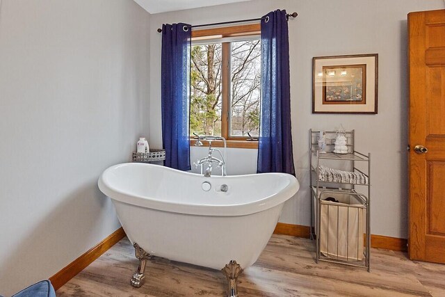 bathroom featuring a soaking tub, baseboards, and wood finished floors