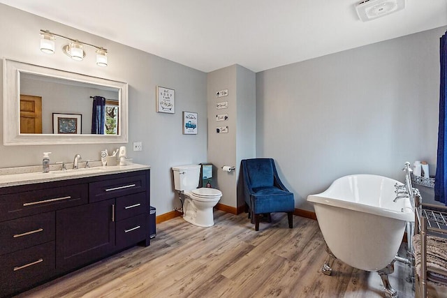 full bath featuring baseboards, toilet, a freestanding tub, and wood finished floors