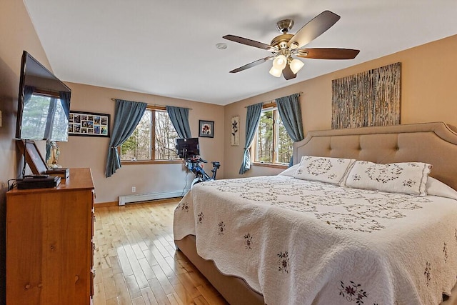 bedroom with baseboards, a baseboard radiator, light wood finished floors, and ceiling fan