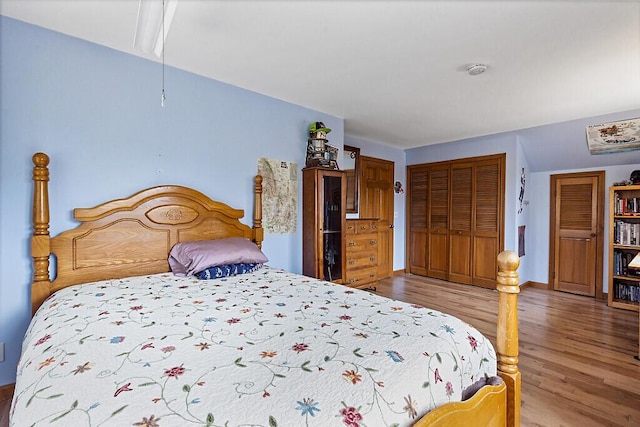 bedroom with baseboards, a closet, attic access, and wood finished floors