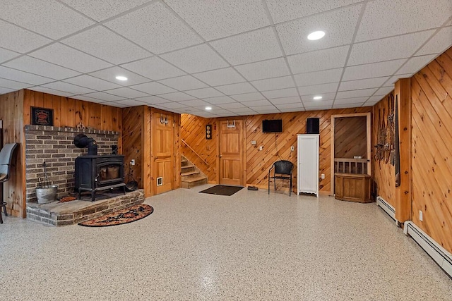 finished below grade area with baseboard heating, a wood stove, wood walls, and stairs