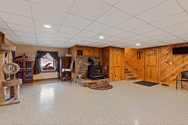 basement with recessed lighting, a wood stove, a drop ceiling, and stairway