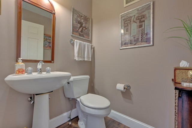 half bathroom with baseboards, wood finished floors, visible vents, and toilet