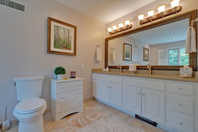 bathroom with visible vents, double vanity, toilet, baseboards, and a sink