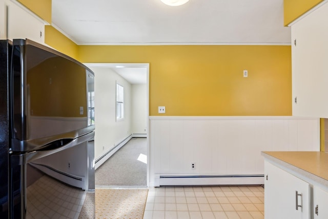 kitchen with freestanding refrigerator, white cabinets, baseboard heating, and a wainscoted wall