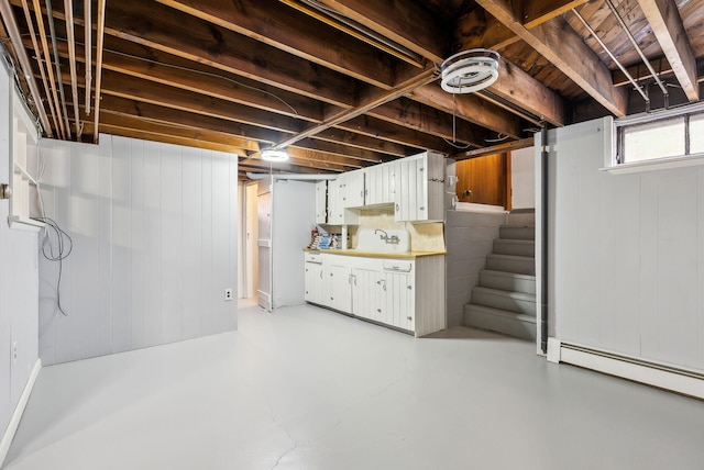 below grade area featuring wooden walls, a sink, stairway, and a baseboard radiator