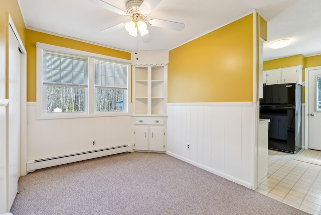 spare room featuring a baseboard radiator, a ceiling fan, wainscoting, and light colored carpet