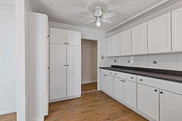kitchen with tasteful backsplash, light wood finished floors, white cabinetry, a ceiling fan, and dark countertops