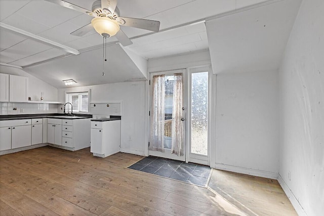 kitchen with light wood-style flooring, a sink, open shelves, dark countertops, and vaulted ceiling with beams