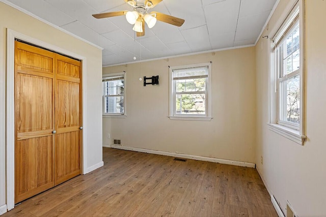 unfurnished bedroom with a closet, visible vents, crown molding, baseboards, and light wood-style floors