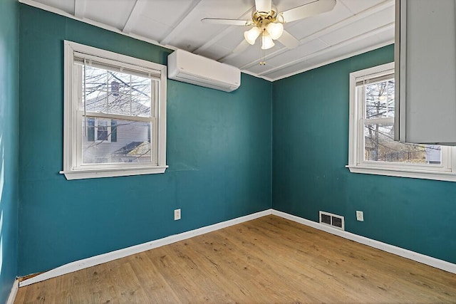empty room with a wealth of natural light, visible vents, a wall unit AC, and wood finished floors