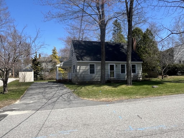 cape cod home with a chimney, a front lawn, and aphalt driveway
