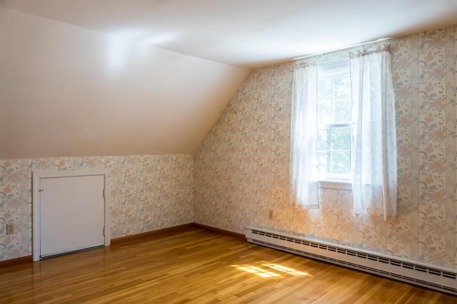 additional living space with wallpapered walls, baseboard heating, lofted ceiling, and light wood-type flooring