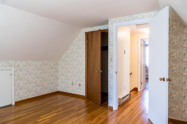 additional living space featuring baseboards, a baseboard radiator, wood finished floors, and wallpapered walls