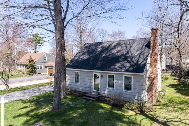 cape cod-style house with roof with shingles, a front yard, and a chimney