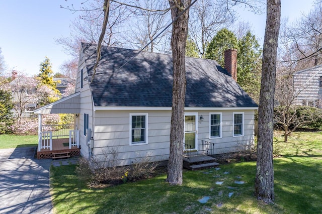 cape cod-style house featuring a shingled roof, a front lawn, a chimney, and a deck
