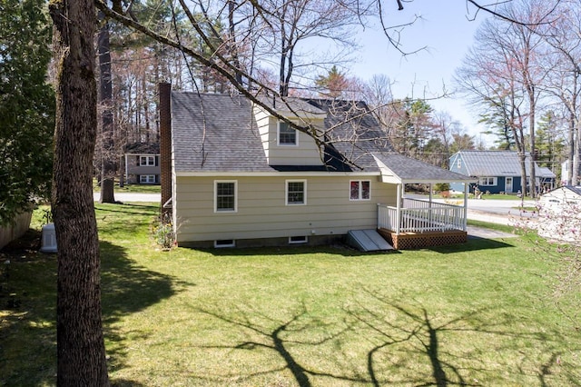 back of house featuring a yard, a chimney, a shingled roof, and a wooden deck