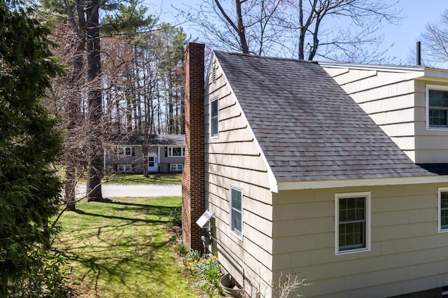view of side of home with a lawn, roof with shingles, and a chimney