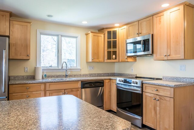 kitchen featuring light brown cabinets, glass insert cabinets, recessed lighting, a sink, and appliances with stainless steel finishes
