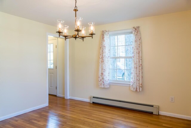 unfurnished dining area featuring baseboards, baseboard heating, wood finished floors, and a chandelier