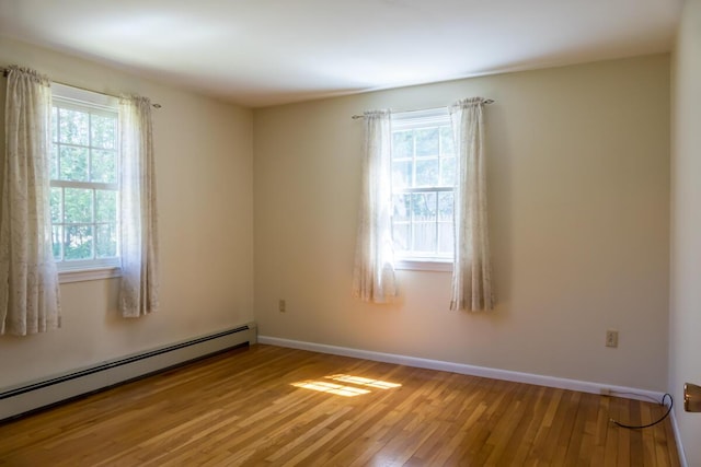 empty room featuring baseboards, a baseboard heating unit, and light wood-style flooring