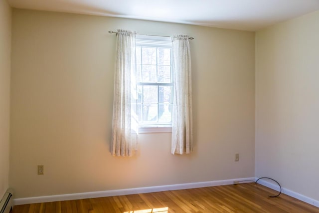 empty room with baseboards, a baseboard radiator, and wood finished floors