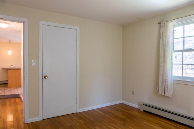 unfurnished room featuring a healthy amount of sunlight, wood-type flooring, and a baseboard heating unit