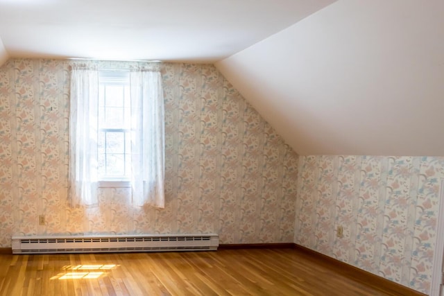 additional living space with wood finished floors, baseboards, wallpapered walls, a baseboard radiator, and vaulted ceiling