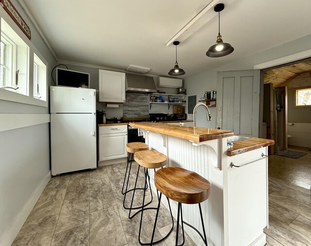 12 Prince Ave, Eastport, ME 04631 - kitchen with butcher block countertops, freestanding refrigerator, wall chimney exhaust hood, pendant lighting, and a breakfast bar