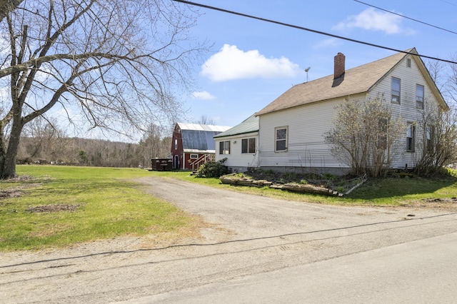 view of property exterior featuring a lawn, dirt driveway, a chimney, and a barn