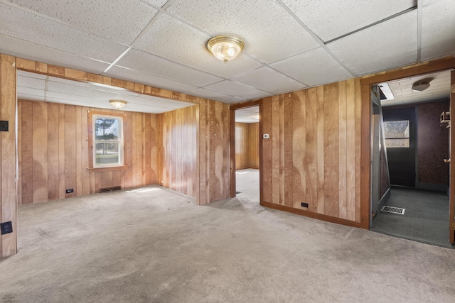 carpeted empty room with wooden walls, visible vents, and a paneled ceiling