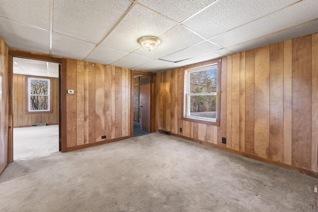 spare room featuring carpet floors, wood walls, a drop ceiling, and visible vents