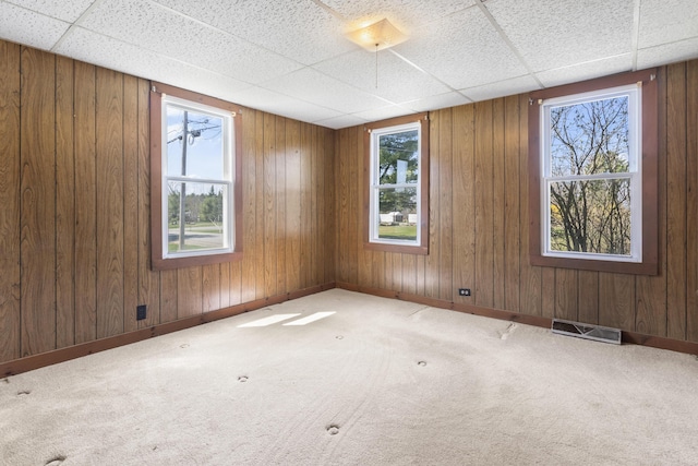 empty room featuring wooden walls, carpet floors, a drop ceiling, and visible vents