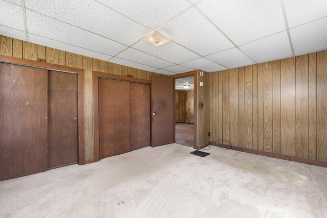 unfurnished bedroom featuring wooden walls, multiple closets, visible vents, and a paneled ceiling