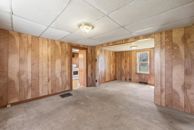 empty room featuring visible vents, carpet flooring, a drop ceiling, and wooden walls